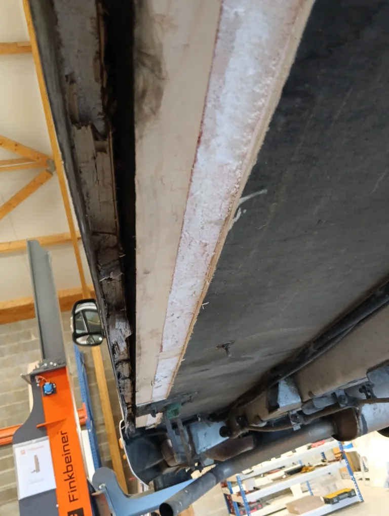 Dessous d'une cellule de camping-car sur colonnes de levage : panneau de plancher en bois et mousse, partie abîmée à gauche