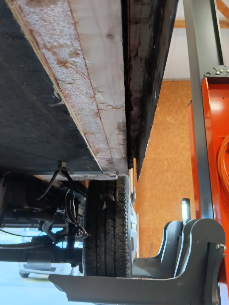 Tranche d'un panneau de plancher en bois et mousse isolante, près d'une roue, véhicule sur colonnes de levage