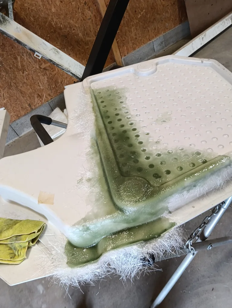 Receveur de douche en fibre en cours de réparation, résine verte et tissu de verre visibles