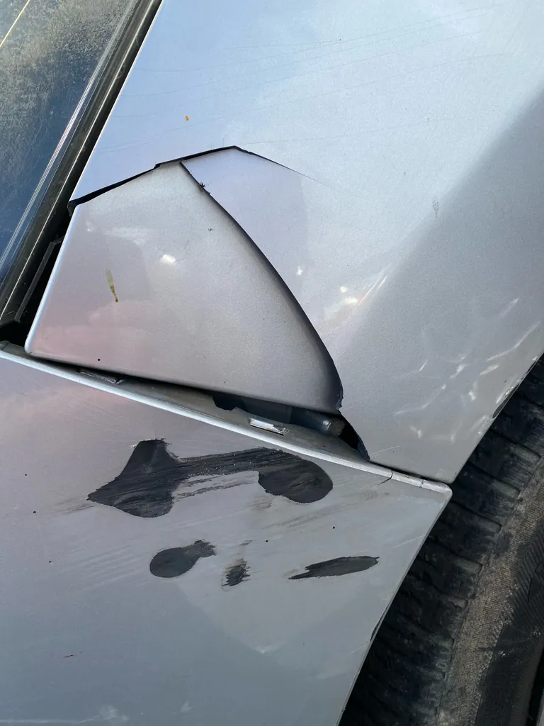 Aile avant d'une voiture grise : tôle fendue et marques noires après un choc